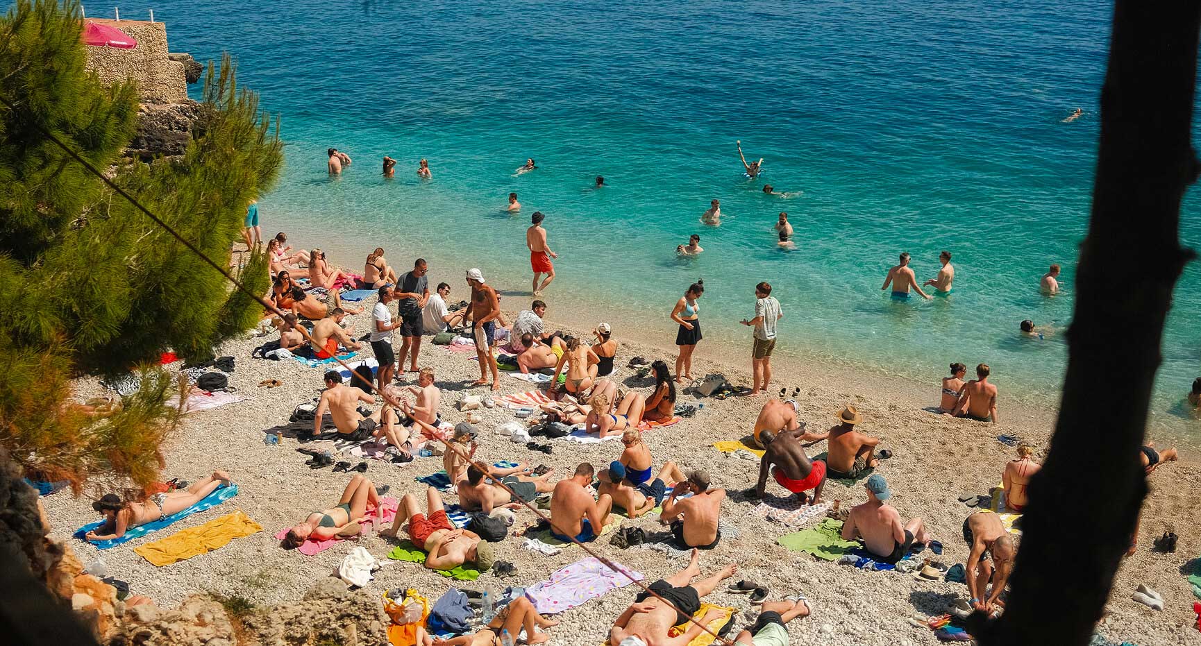 People relaxing and swimming beside turquoise water in a photograph from Kala’s official festival website in Dhërmi, Albania.